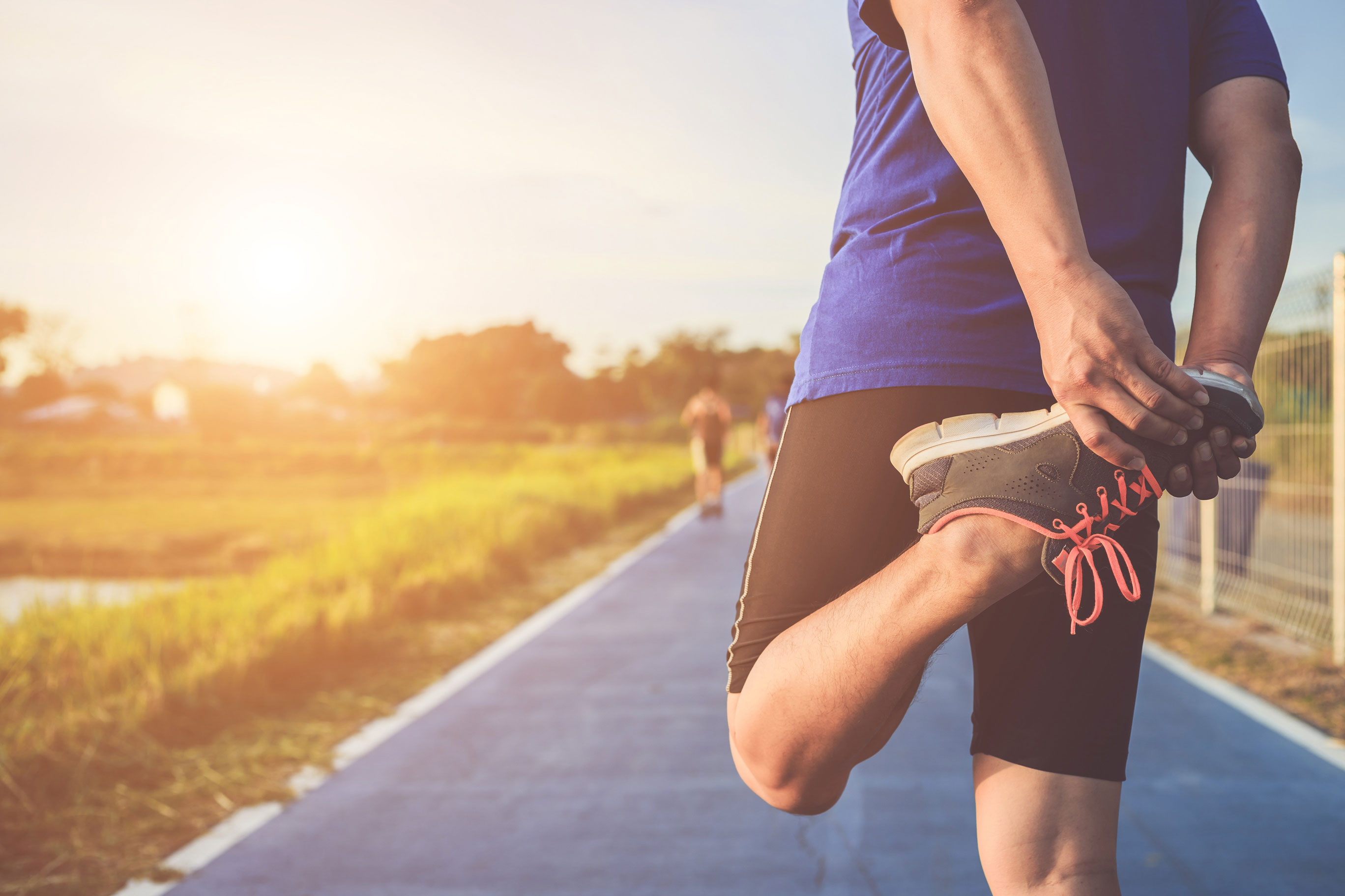 a man stretching his quadriceps and getting ready to go for a run at dusk on a paved pathway